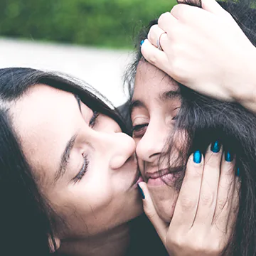 Mother kissing her teen daughter’s cheek