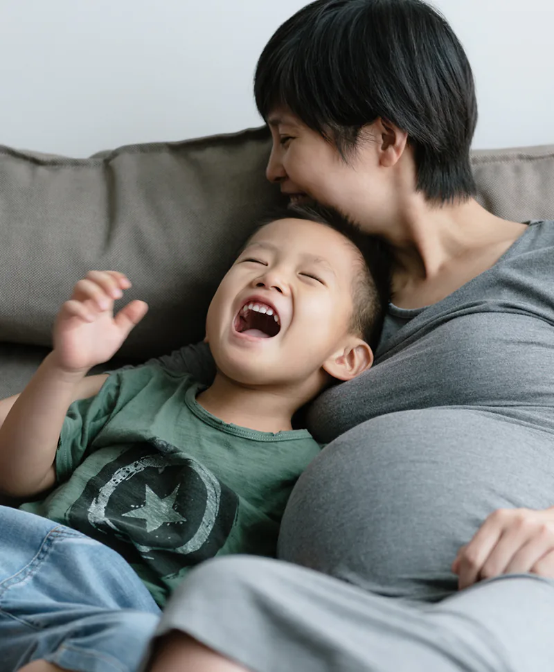 Expecting mother sharing a laugh with her young son sitting on a couch